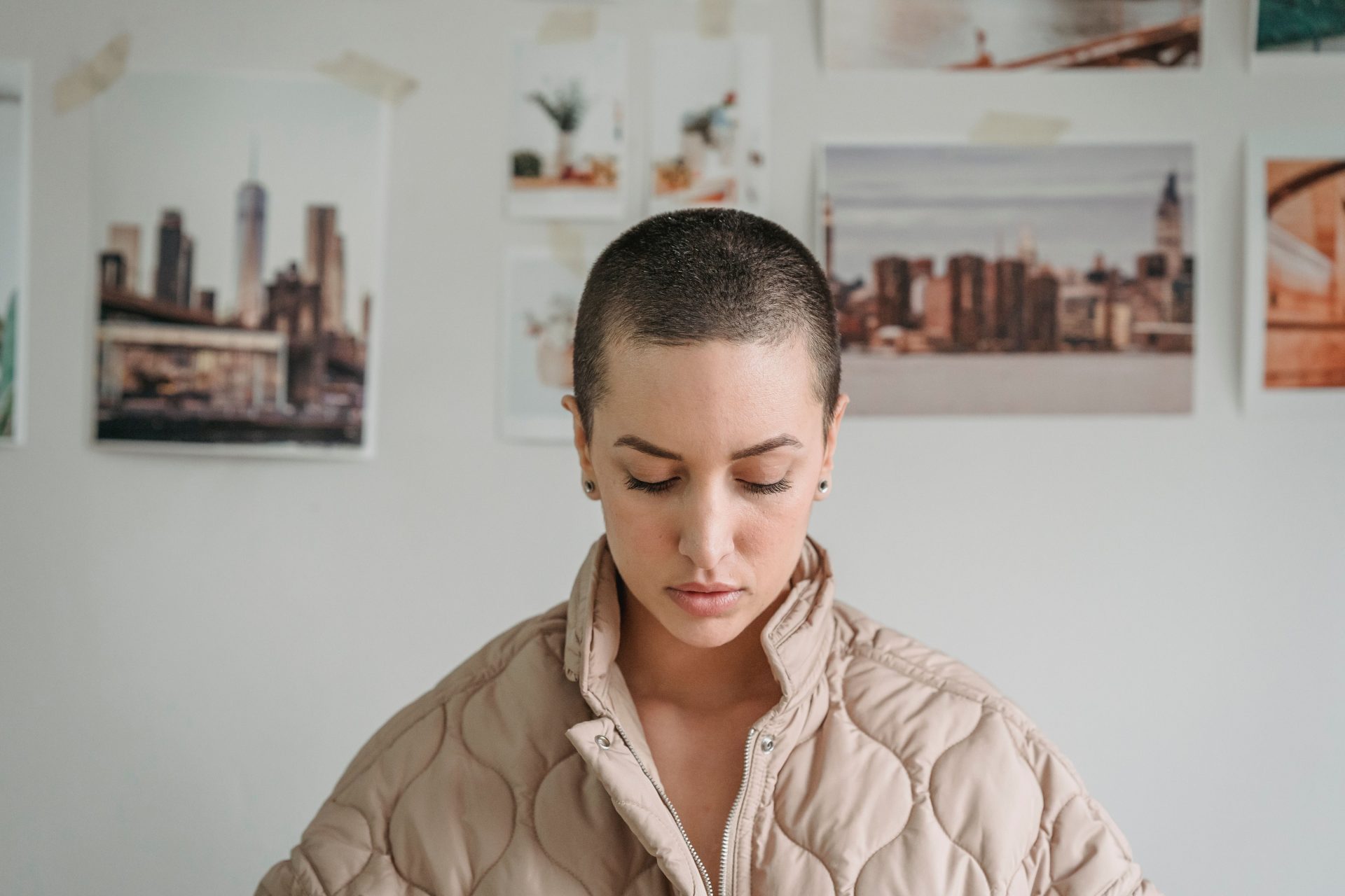 Short haired serene female with makeup looking down against decorative images hanging on white wall